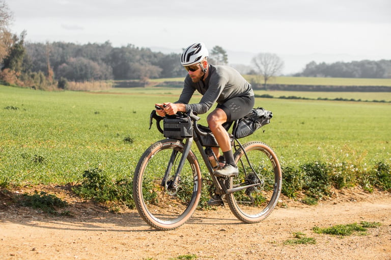 Christian Meier rides the bag-laden Belle Cycles A.T.E.R. along a dirt track between green fields.