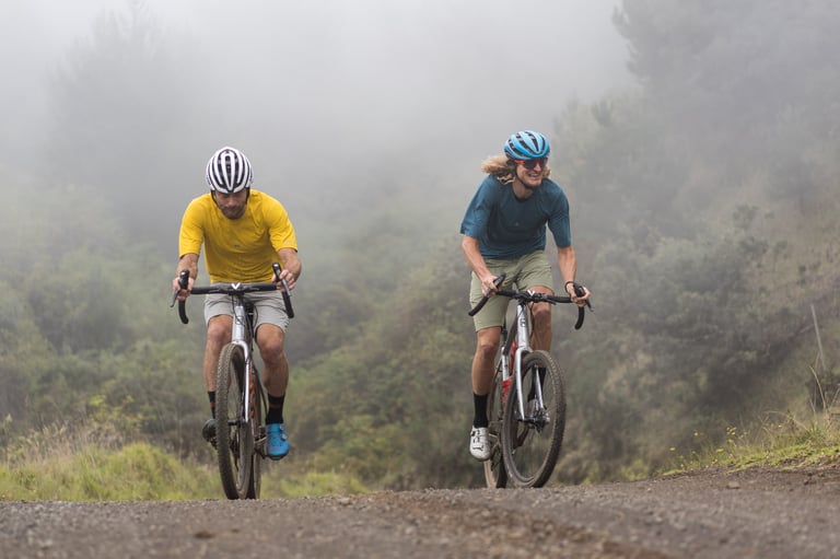 Barry Wicks and Erik Tonkin ride Kona Libre gravel bikes up a misty dirt road on Maui, Hawaii.