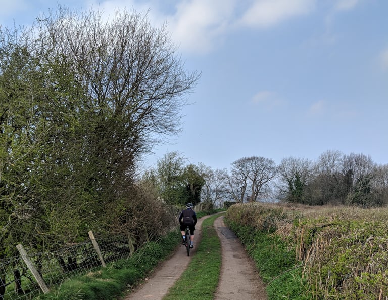 Rider on a gravel bike follows a grassy double-track lane between hedgerows on a Dirty Devil route in the Wye Valley.