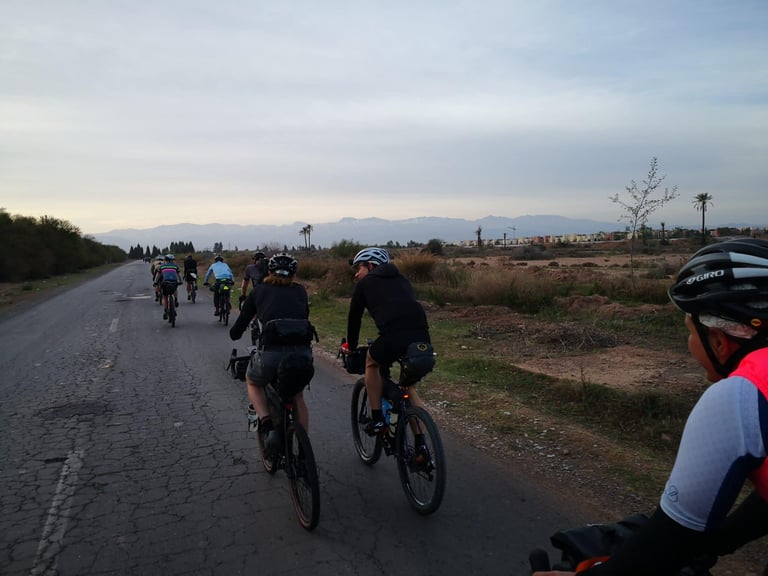 Atlas Mountain Race peloton on a cracked road out of Marrakech, with the snowy Atlas peaks on the horizon.