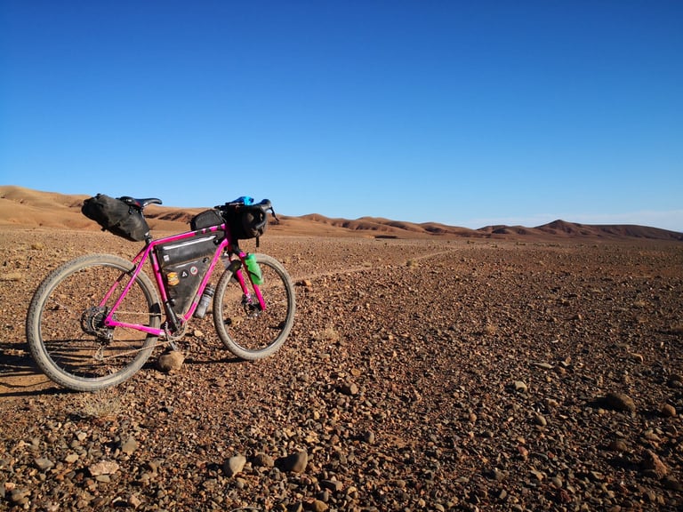 Pink Salsa Cutthroat propped in a stony Moroccan desert under a clear sky on day two of the Atlas Mountain Race.