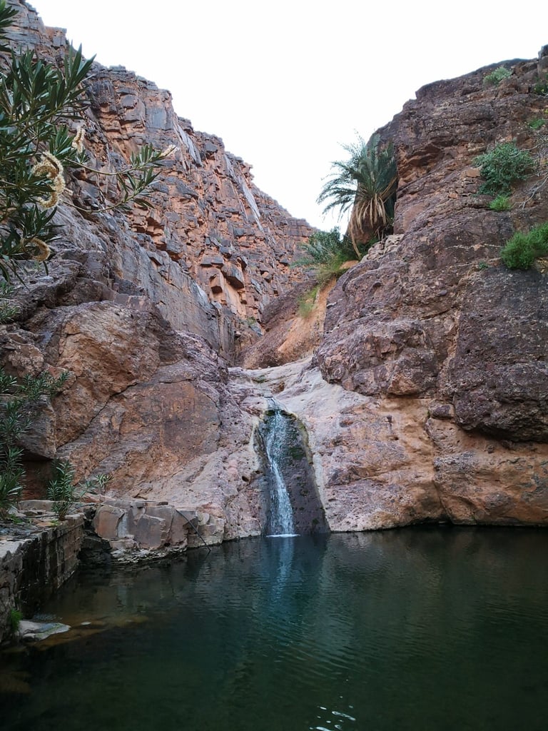 Cascade de Tizgui waterfall dropping into a pool between red rock walls on day three of the Atlas Mountain Race.