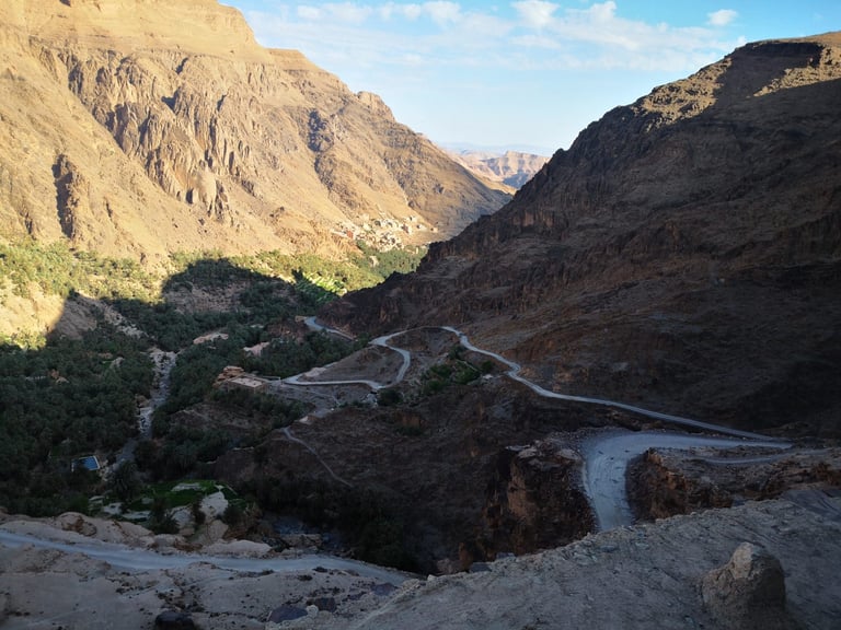 Tarmac hairpins drop into a palm-filled valley below rocky cliffs at Aguinane, on the Atlas Mountain Race route in Morocco.