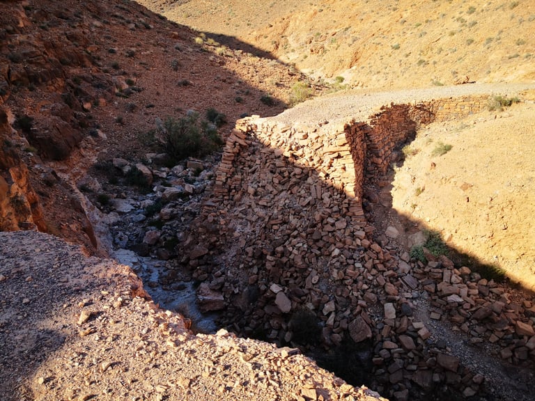 Collapsed stone-built road section above a dry stream bed on the Atlas Mountain Race route in Morocco.