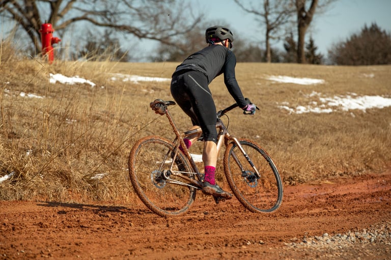 Rider seen from behind powers the mud-splattered Salsa Stormchaser round a bend of red dirt in Oklahoma.