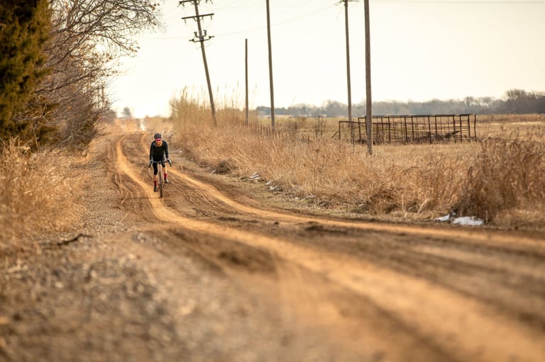 Distant rider on a Salsa Stormchaser along a rutted Oklahoma dirt road lined with power lines and fences.