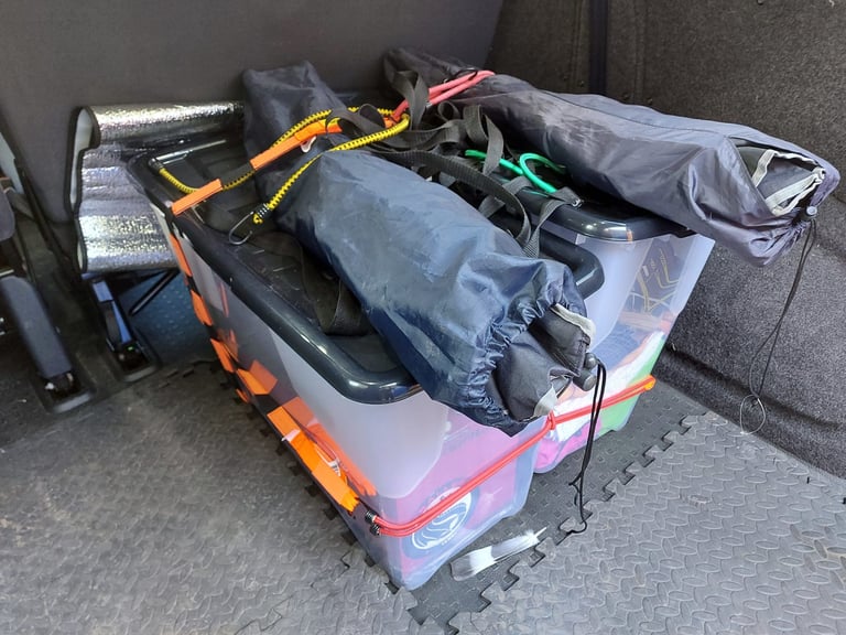 Bagged camping kit and plastic storage boxes in a van boot, held down with Wraptie straps and bungees.