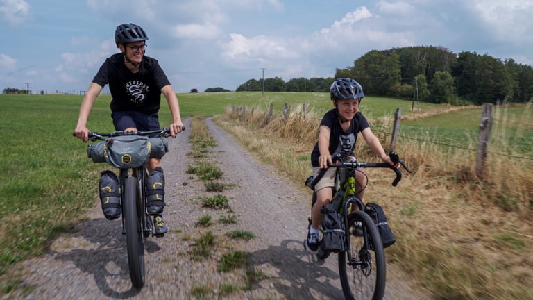 Lubin on his loaded Bombtrack Beyond Junior rides a gravel track between fields alongside his father Clem.