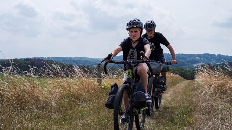 Seven-year-old Lubin rides a bag-laden Bombtrack Beyond Junior along a grassy ridge track, Clem close behind.