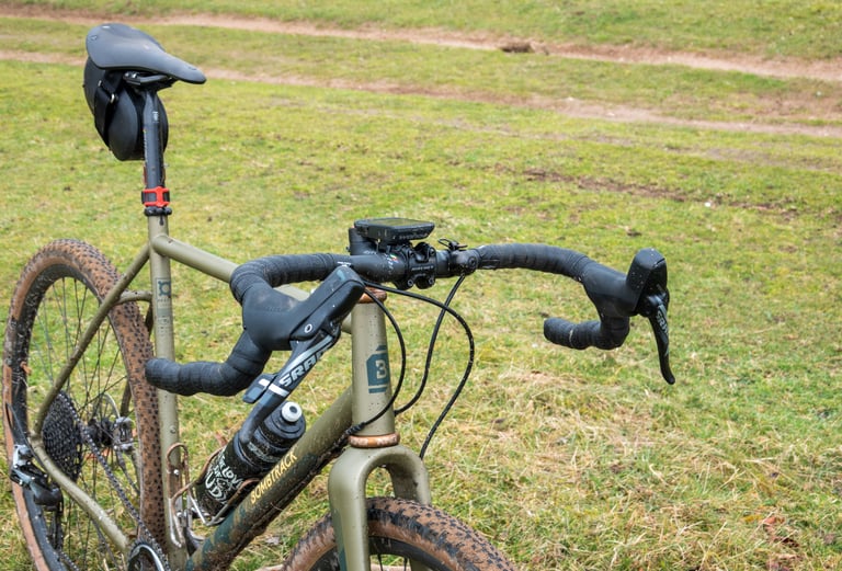 Mud-splashed Ritchey WCS Carbon VentureMax on a Bombtrack Hook EXT with a seat pack, standing on grass.
