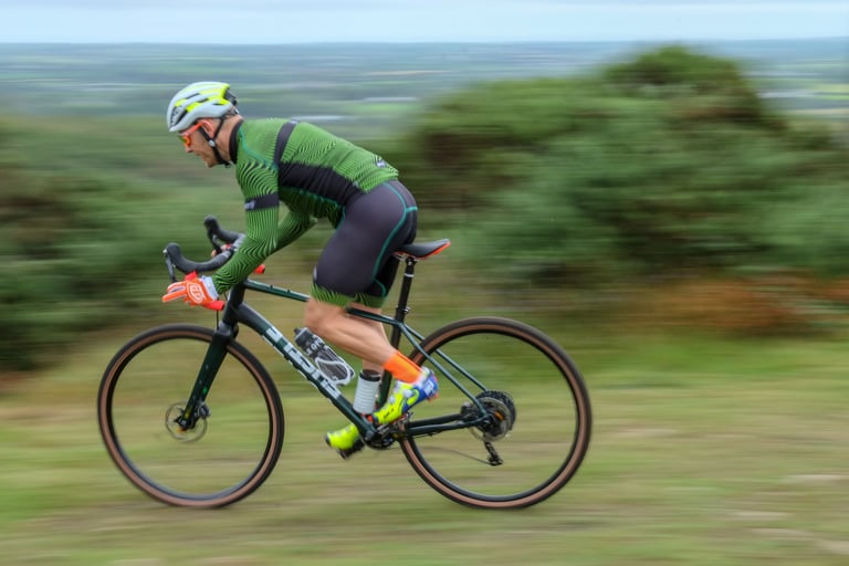 Rider in green kit sprints a FUSTLE Causeway GR1 across open moorland, the panned background blurred.