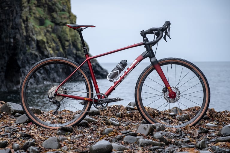 Side view of the red FUSTLE Causeway GR1 and its dropped top tube, parked on a pebble beach by the sea.