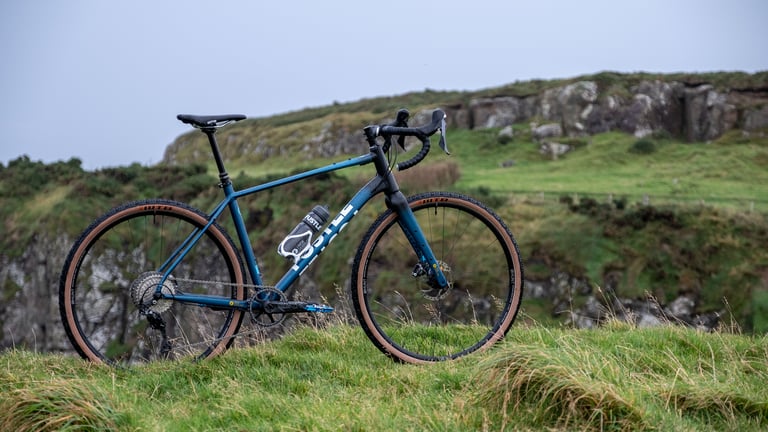 FUSTLE Causeway GR1 in blue on a grassy clifftop, with a water bottle in the main triangle.
