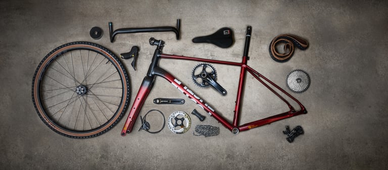 Flat-lay of FUSTLE Causeway GR1 parts: frame, fork, wheel, Shimano GRX cranks, bars, saddle and cassette.