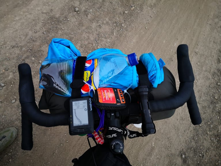 View over the bars of a gilet and two bottles strapped on top of the handlebar harness, with a Wahoo computer below.
