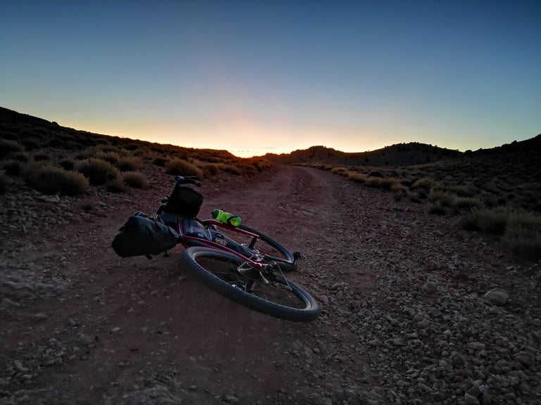 Loaded bike lying on a red dirt track at sunrise on day two of the Atlas Mountain Race in Morocco.