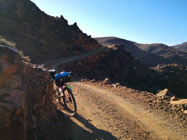 Loaded gravel bike propped against rocks on a stony mountain track during the Atlas Mountain Race.