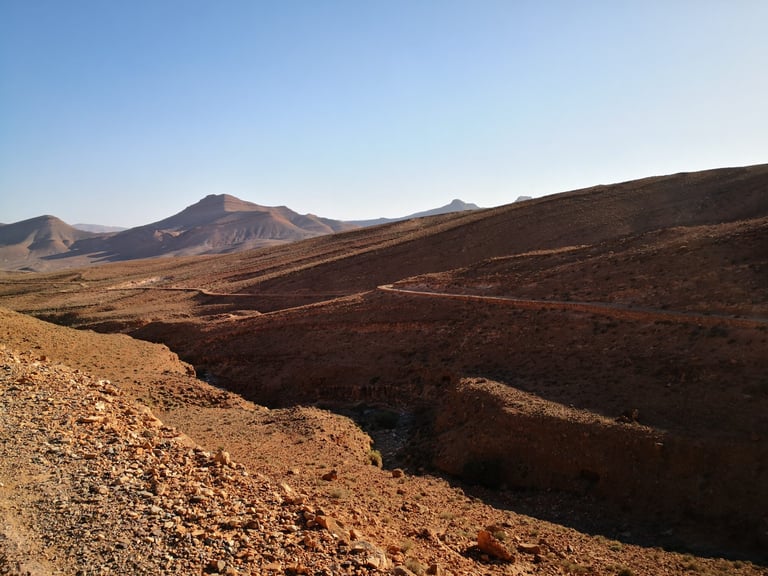 Narrow road snakes across barren hills towards distant peaks on the Atlas Mountain Race route in Morocco.