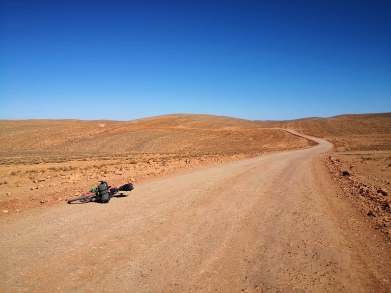 Loaded bike lies beside a smooth gravel road curving through open desert hills on the Atlas Mountain Race.