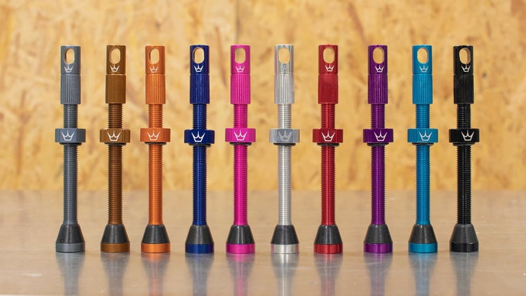 Ten Peaty's tubeless valves in a row of anodised colours, from grey and bronze through pink, red, purple and blue to black.