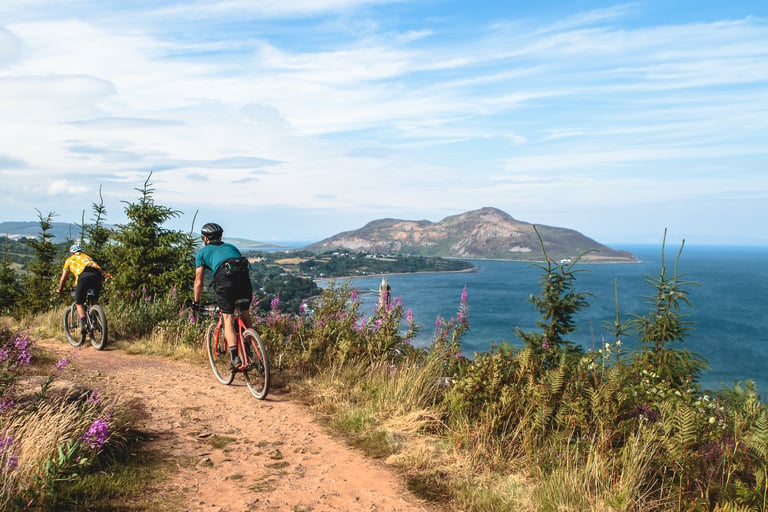 Two riders on gravel bikes on a coastal dirt path above the sea at Grinduro on the Isle of Arran.