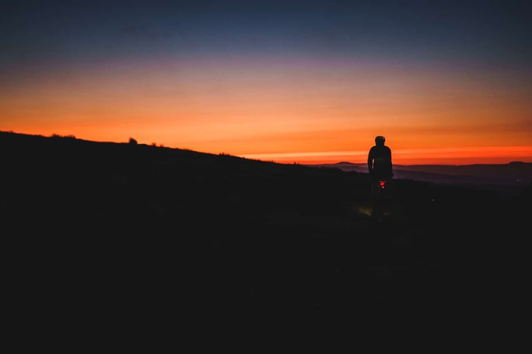 Tom Probert rides in silhouette against an orange sunset on the Old Coal Road, Lancashire, during the GBDURO.
