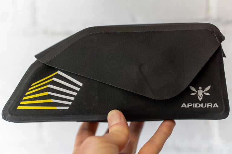 Apidura Racing Top Tube Bag held in one hand, closed, showing its yellow and silver reflective print.