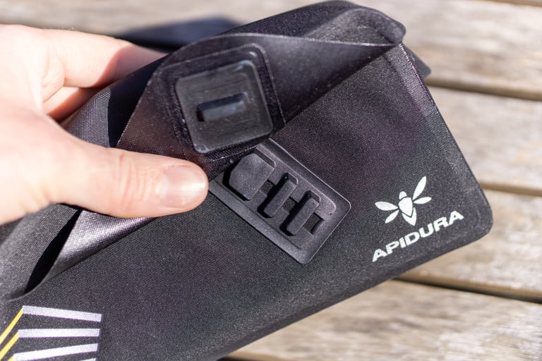 Magnetic catch on the underside of the Apidura Racing top tube bag's flap, held open by a thumb.