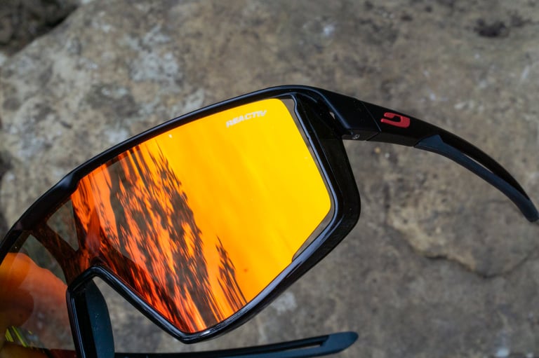 Close-up of the orange mirrored Reactiv photochromic lens on the Julbo Fury sunglasses, lying on grey rock.