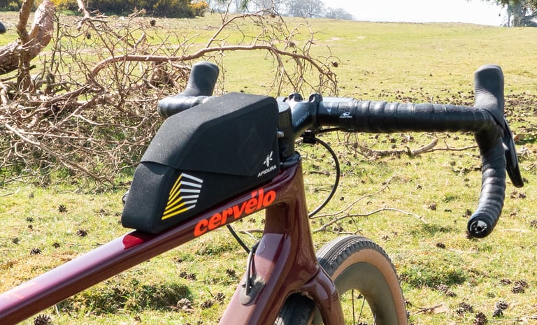 Apidura Racing top tube bag fitted just behind the stem of a Cervélo drop-bar bike parked on grass.