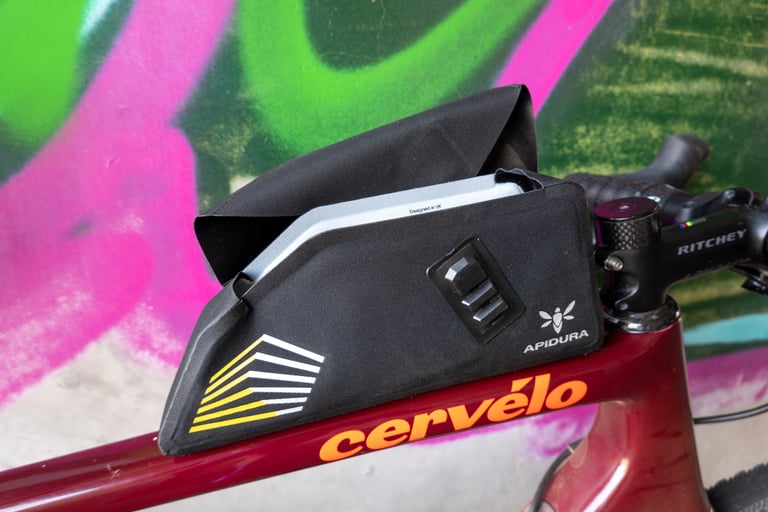 Apidura Racing top tube bag with the flip-top cover open, mounted on a Cervélo frame beside a Ritchey stem.