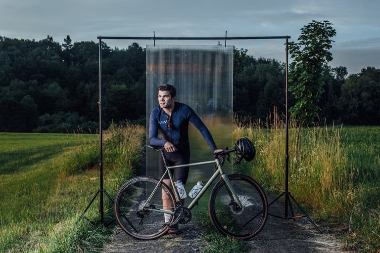 Rider leans on a green Repete Cycles Verne in front of a clear panel at the edge of a field.