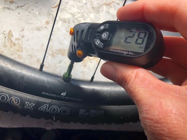 Topeak SmartGauge D2 reading 28 psi, its head pressed onto the Presta valve of a 700 x 40C gravel tyre.
