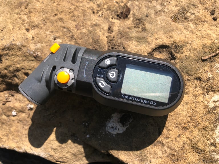 Topeak SmartGauge D2 lying on a rock in sunshine, orange valve switch and bleed button beside the blank display.