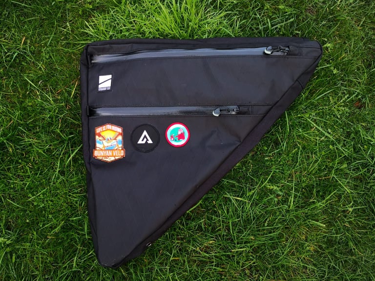 Drive side of the Straight Cut Design custom frame bag laid on grass, with two zipped compartments and three patches.