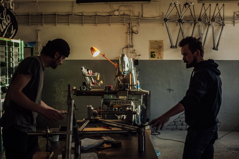 Two framebuilders at work in the Repete Cycles workshop in Prague, frames hanging on the wall behind.