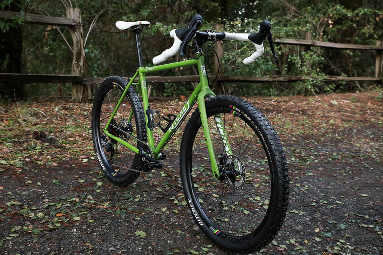 Ritchey Outback V2 in green with white bar tape and a large knobbly front tyre, from a low front three-quarter angle.