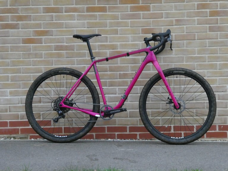 Pink Salsa Cutthroat V2 gravel bike with drop bars against a brick wall, before the custom frame bag was fitted.