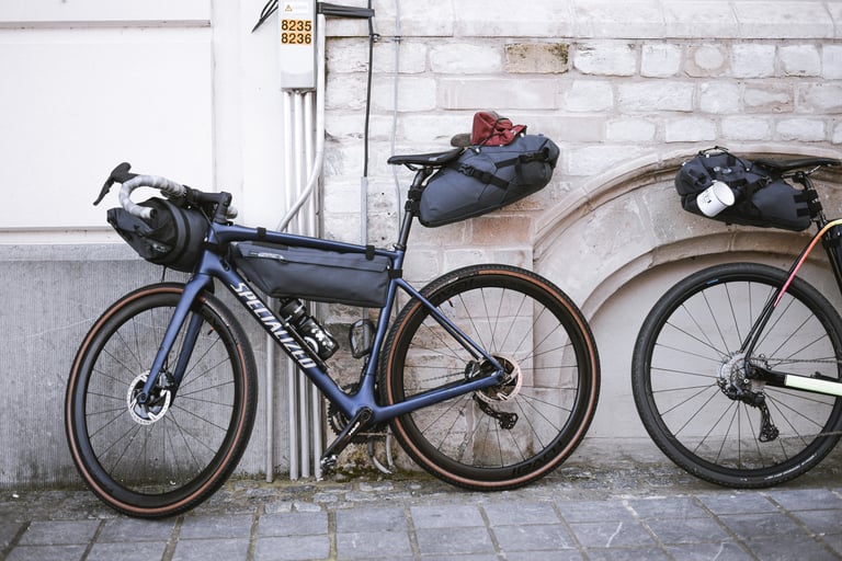 Blue Specialized Diverge gravel bike with handlebar, frame and saddle bags leaning against a pale brick wall.