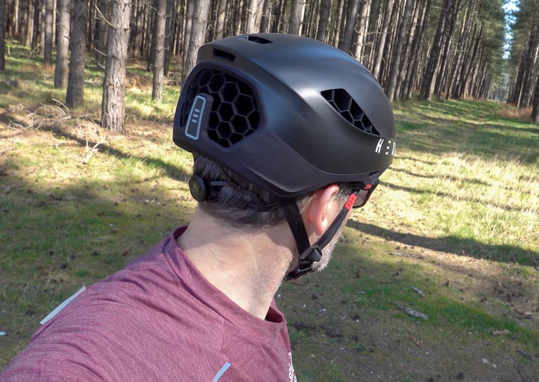 Rear three-quarter view of the HEXR helmet on a rider, with the honeycomb rear port and tensioner dial.
