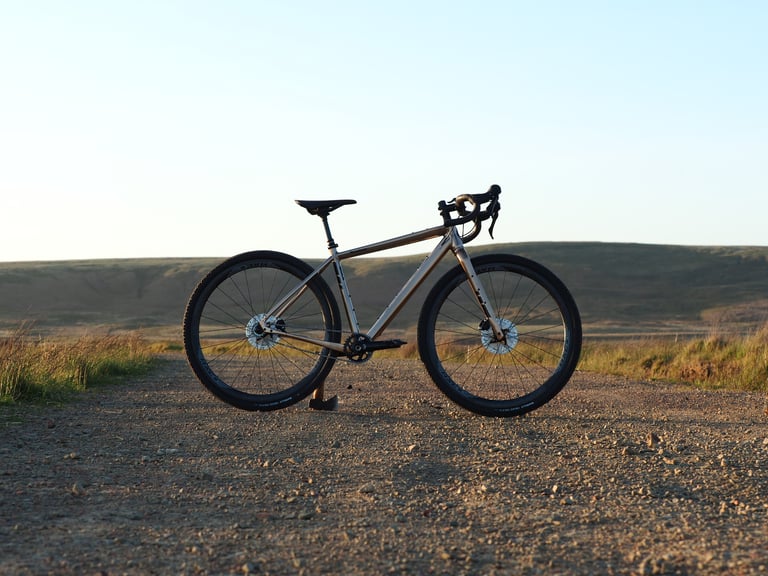 Keep Pedalling's Salsa Stormchaser singlespeed on a gravel track at sunset with moorland behind.