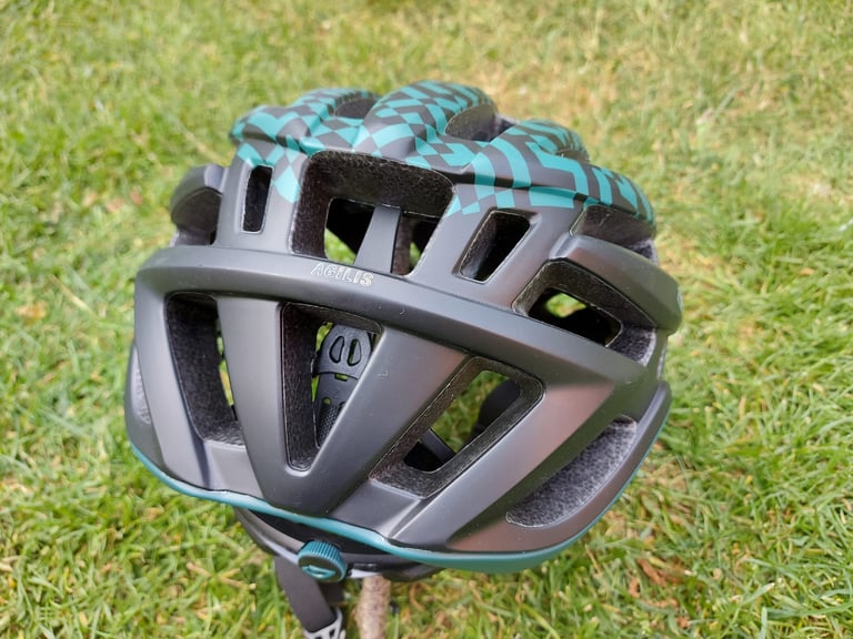 Rear view of the Giro Agilis helmet on grass, showing the low-cut back, Agilis lettering and teal fit dial.