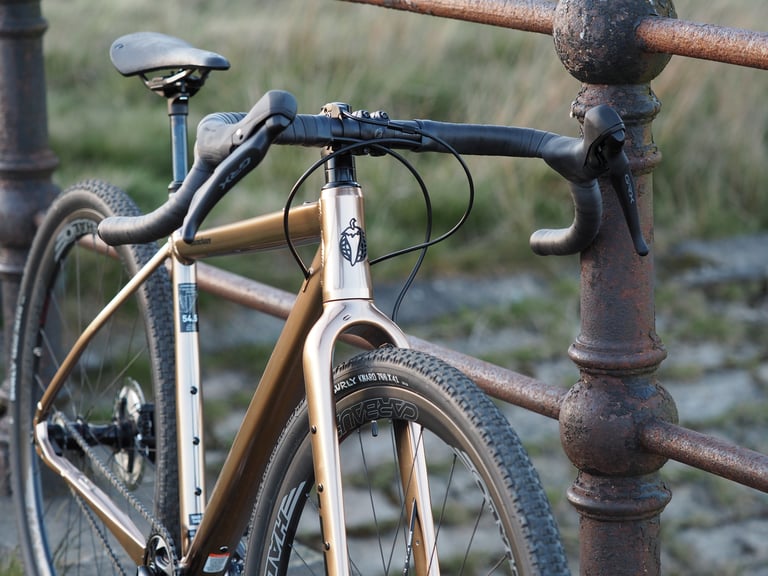 Front end of the Salsa Stormchaser against rusty railings, with GRX levers, Cowchipper bars and Surly Knard tyre.