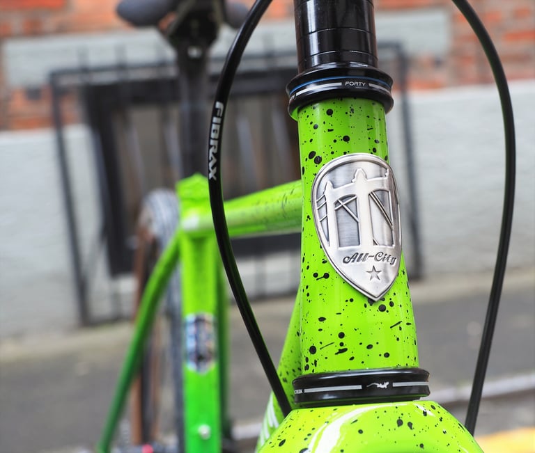 All City badge on the head tube of the green splatter-paint Nature Boy, with a Cane Creek headset.