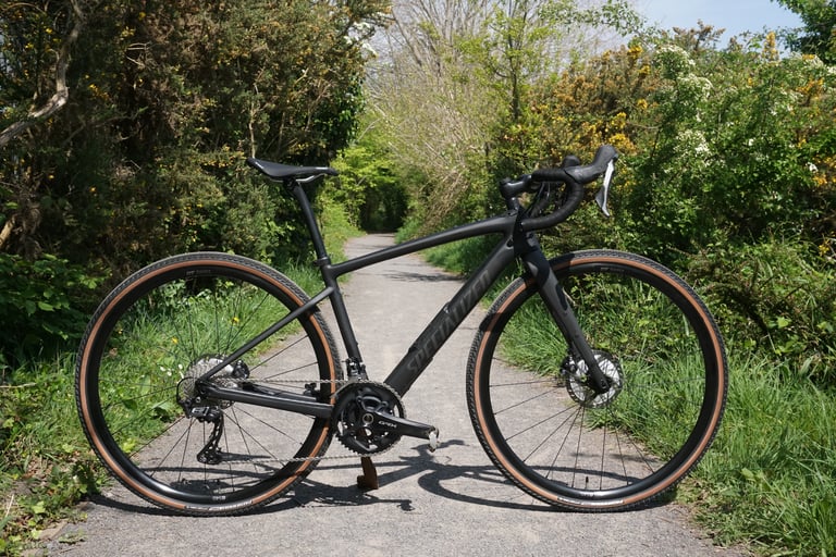 Side view of the matte black Specialized Diverge Comp Carbon with tan-wall tyres on a tree-lined lane.