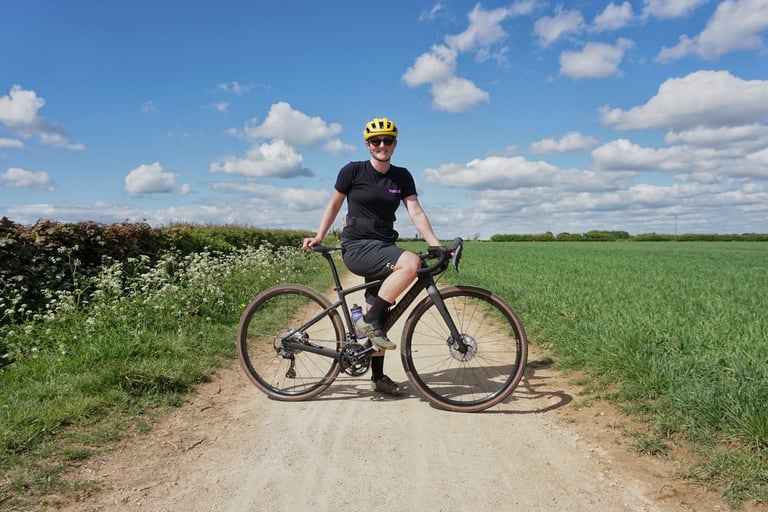 Reviewer Katherine Moore poses on the Specialized Diverge Comp Carbon on a dry gravel track beside green fields.