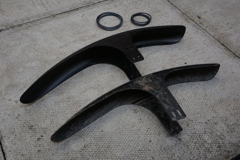 New Gravelhugger front guard laid on paving beside a mud-caked prototype, with the o-rings used to fit it.
