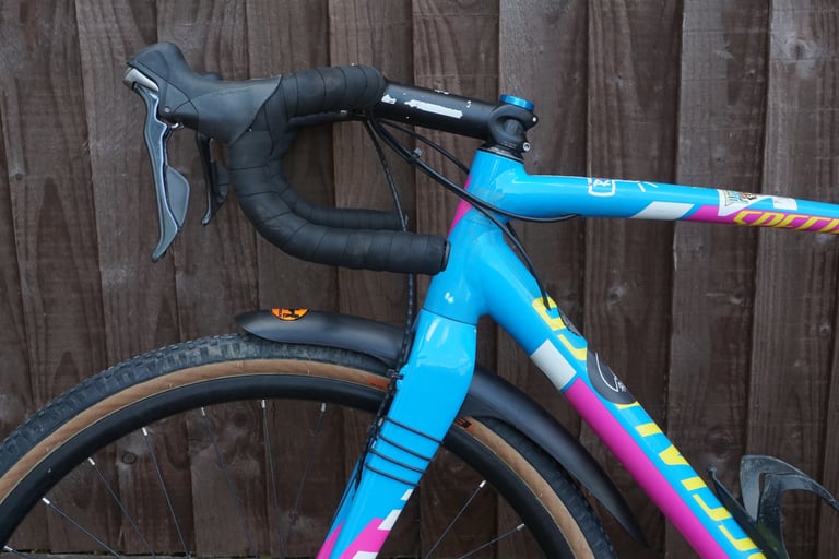 Front Gravelhugger mudguard tucked under the fork crown of a blue gravel bike, seen side-on with drop bars.