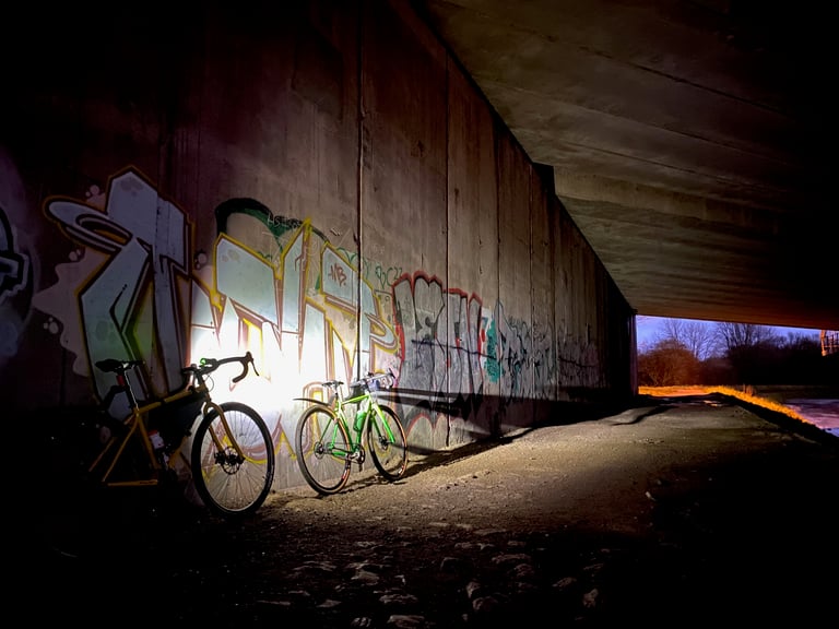 Two gravel bikes lit against a graffiti-covered underpass wall at night, during the reverse Rapha Prestige ride.