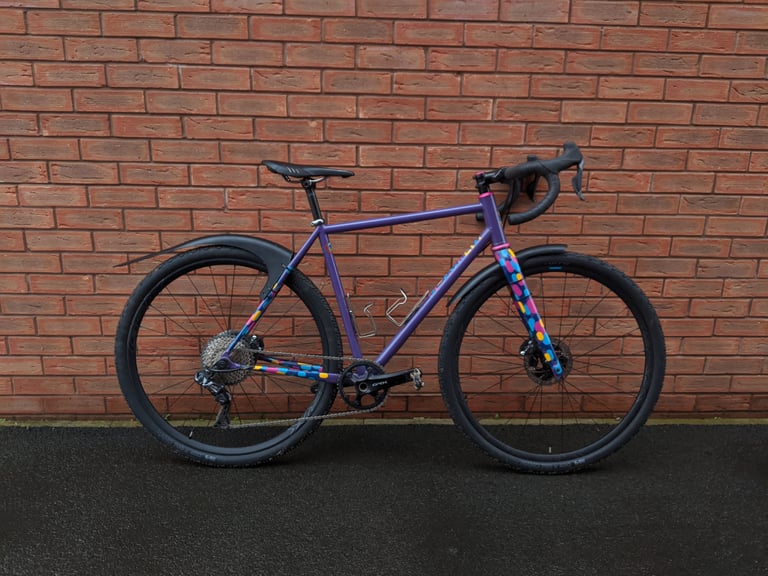 Gravelhugger front and rear mudguards fitted to a purple steel gravel bike against a red brick wall.